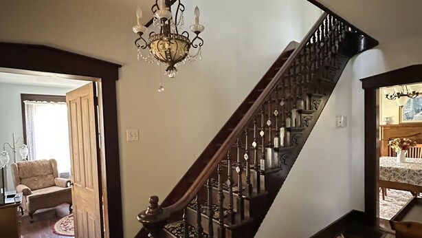 Una imponente escalera con candelabro, barandillas de madera y alfombra roja.