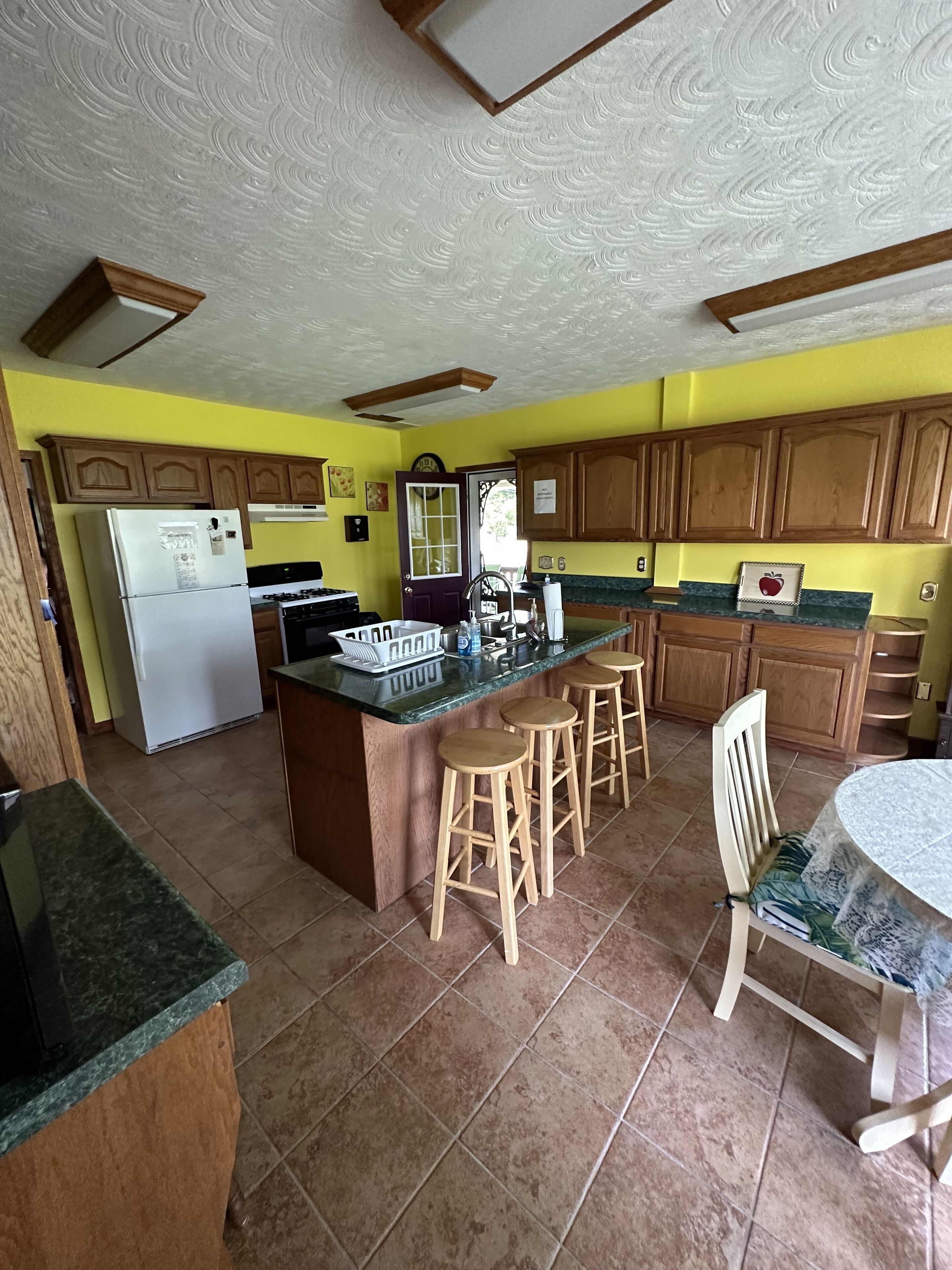 A kitchen with wooden cabinets, a central island with stools, a refrigerator, and a stove.