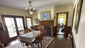 Un comedor con una mesa grande, sillas y un tapete. Hay una chimenea, un candelabro y vistas al exterior.