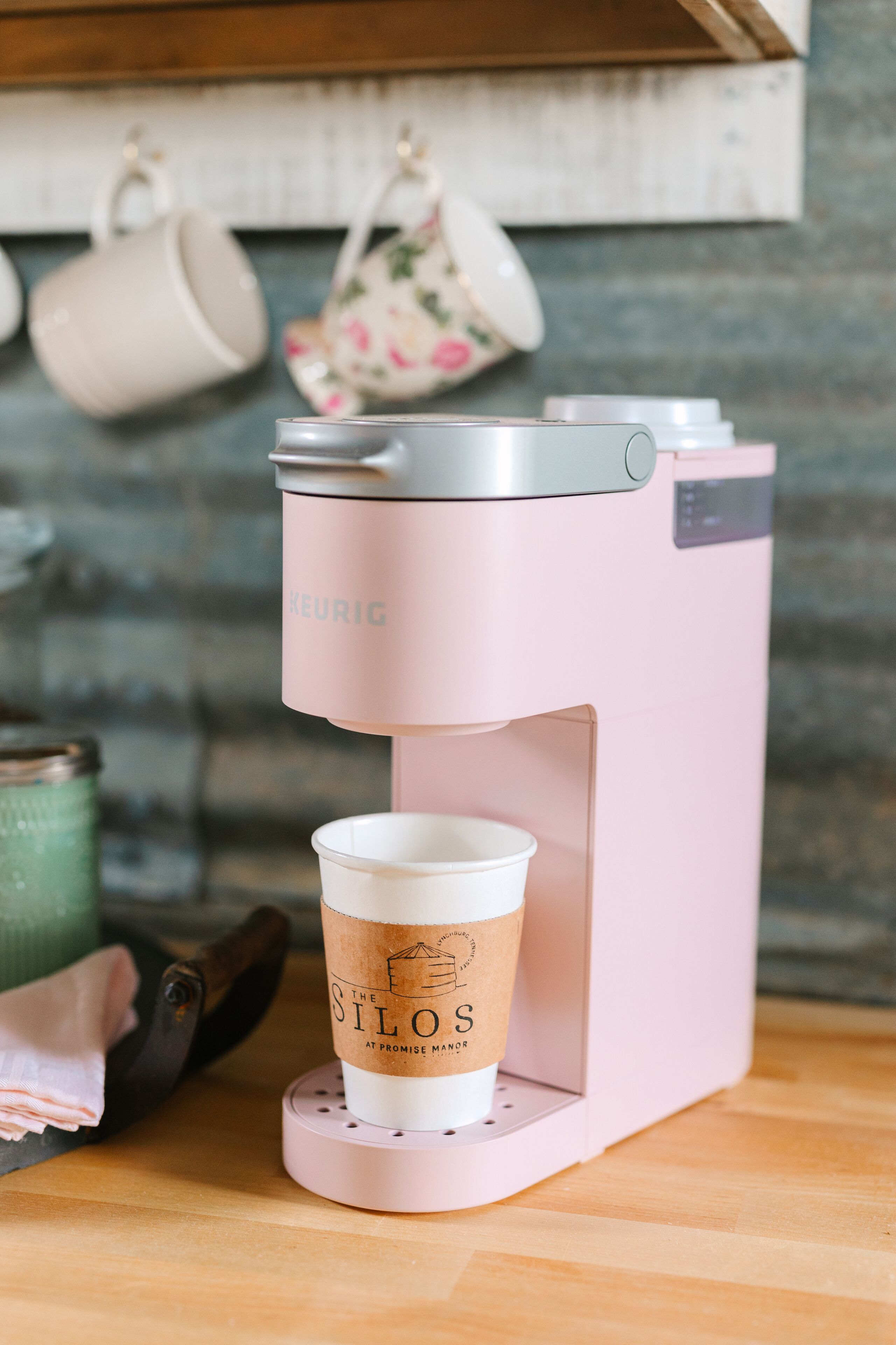 Una cafetera Keurig rosa con una taza desechable que dice "The Silos at Promise Manor" en su base.