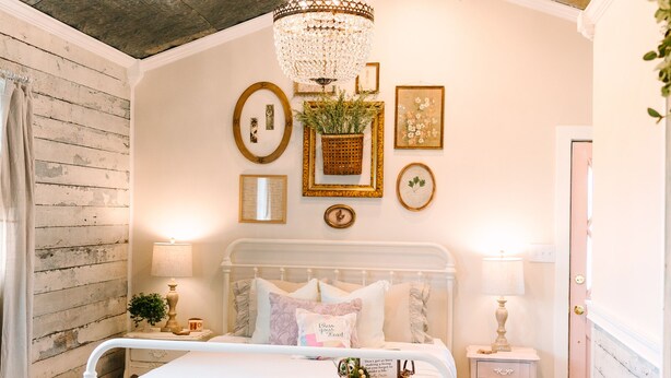 Een slaapkamer met een wit bed, houten balken in het plafond, een kroonluchter en decoratie aan de muur.