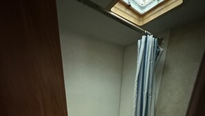 Een kleine badkamer met toilet, douche en een dakraam boven het toilet.