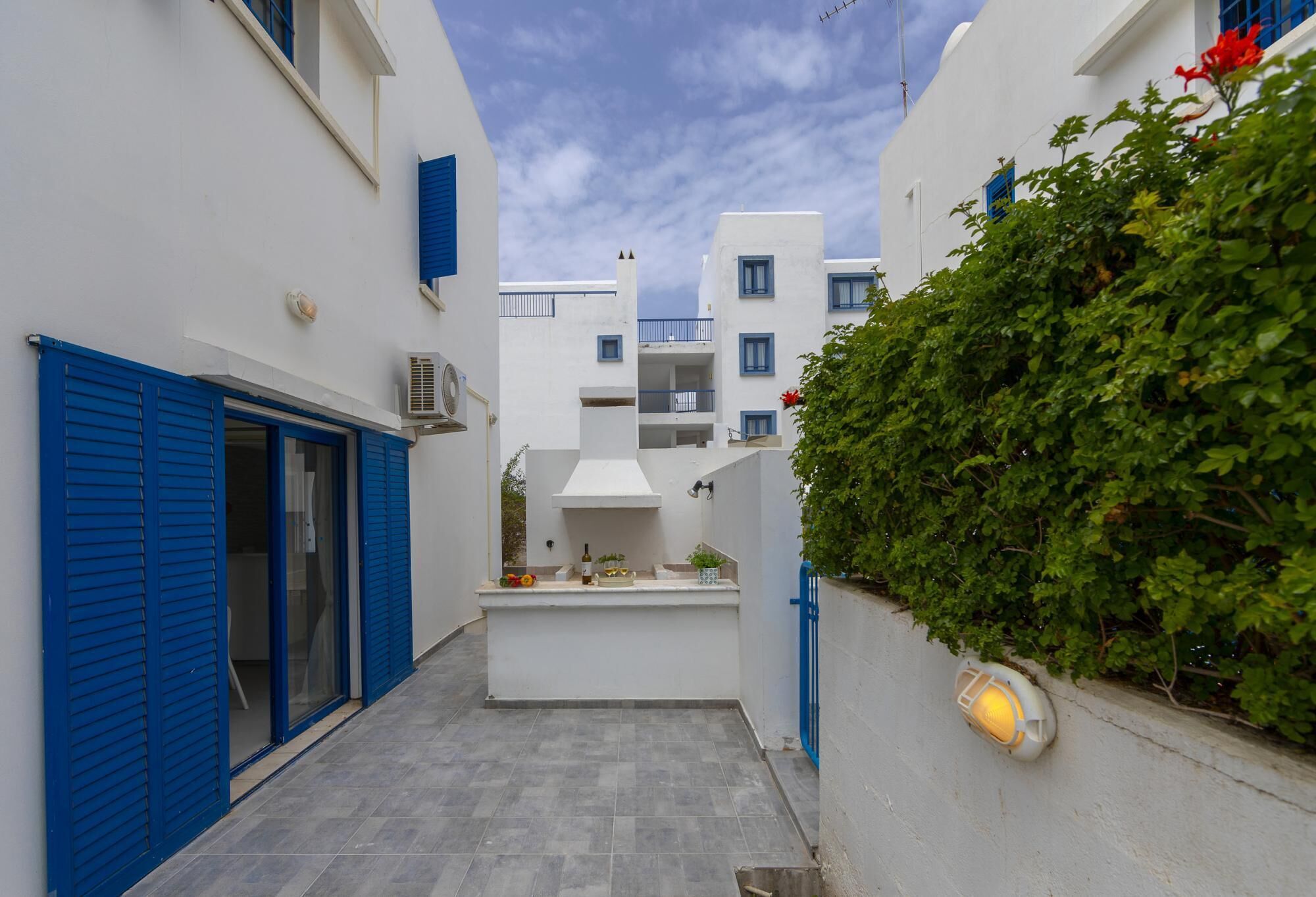 Un callejón estrecho con edificios blancos, contraventanas azules y una pequeña cocina al aire libre.