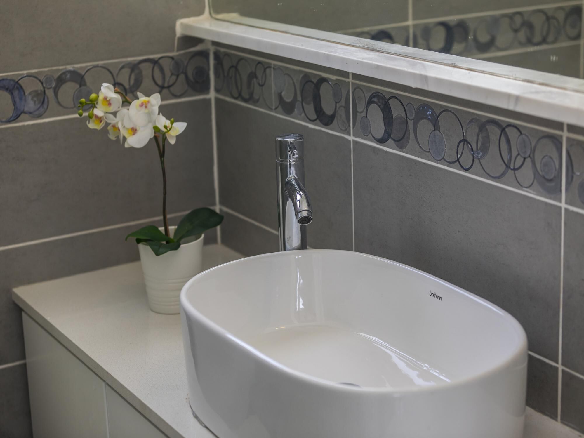 Un bagno con un lavandino bianco, un rubinetto moderno e piastrelle decorative.