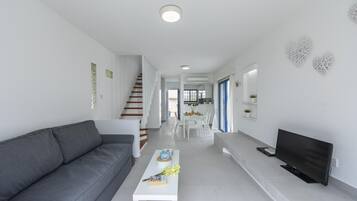 Ein modernes Wohnzimmer mit grauem Sofa, weißem Couchtisch und einem Flachbildfernseher.