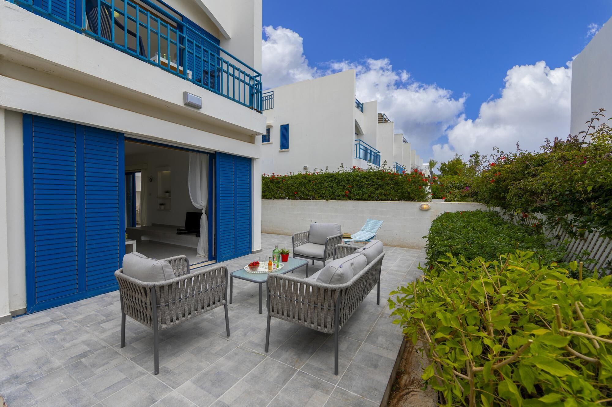 A patio with wicker furniture and a table, a blue door, and a white building with blue railings.
