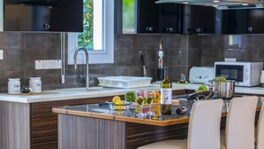 Une cuisine moderne avec un îlot central, des tabourets de bar, une bouteille de vin et un four à micro-ondes.