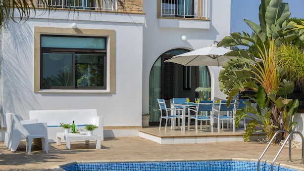 A modern pool area with a tiled pool, white outdoor furniture, and a large umbrella. - Villa Alexa Protaras (Paralimni)
