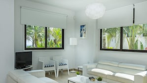 A modern living room with a flat-screen TV, white sofas, a coffee table, and large windows with a view of greenery. - Villa Alexa Protaras (Paralimni)