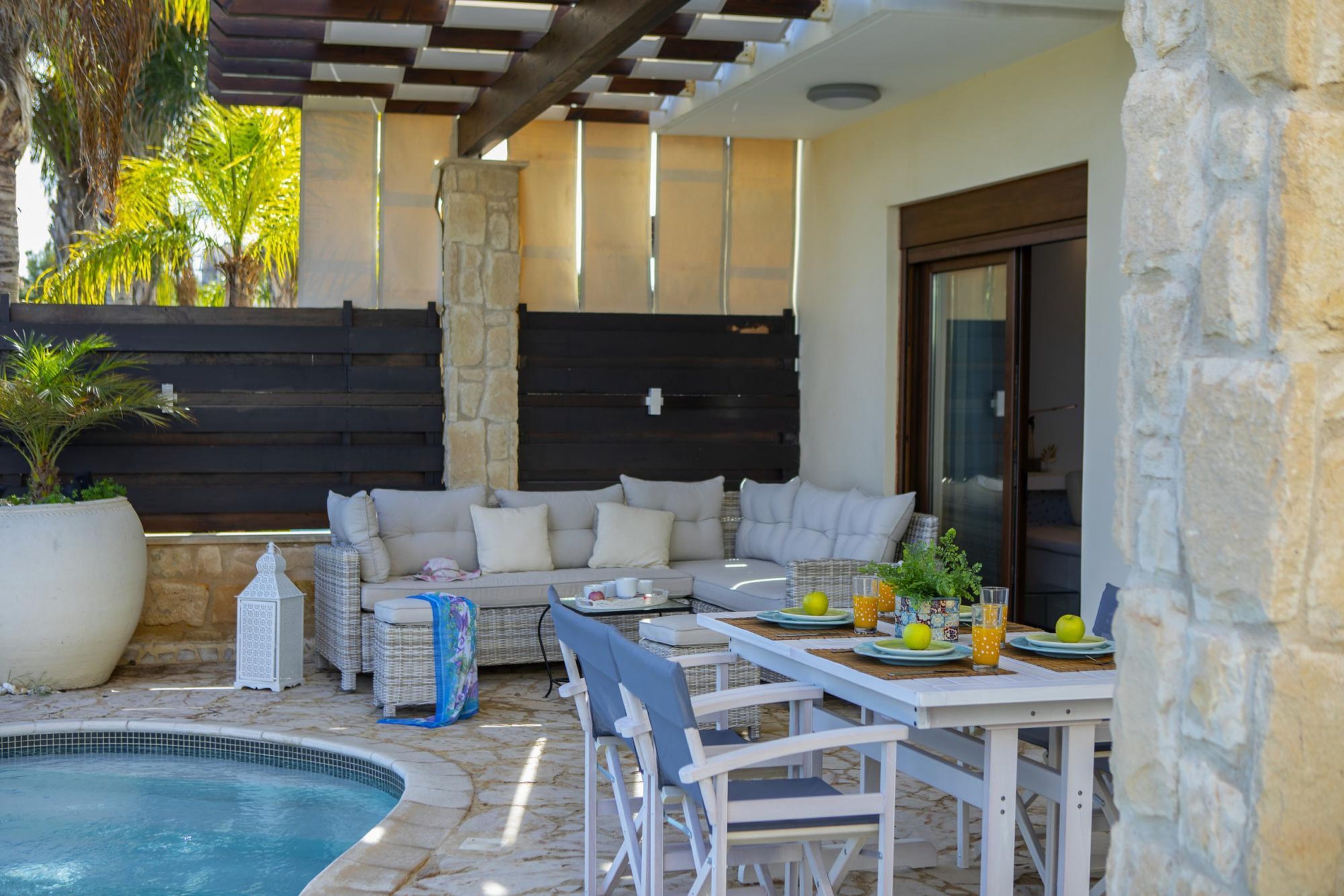 A poolside area with a stone wall, a sofa, and a dining table with chairs.