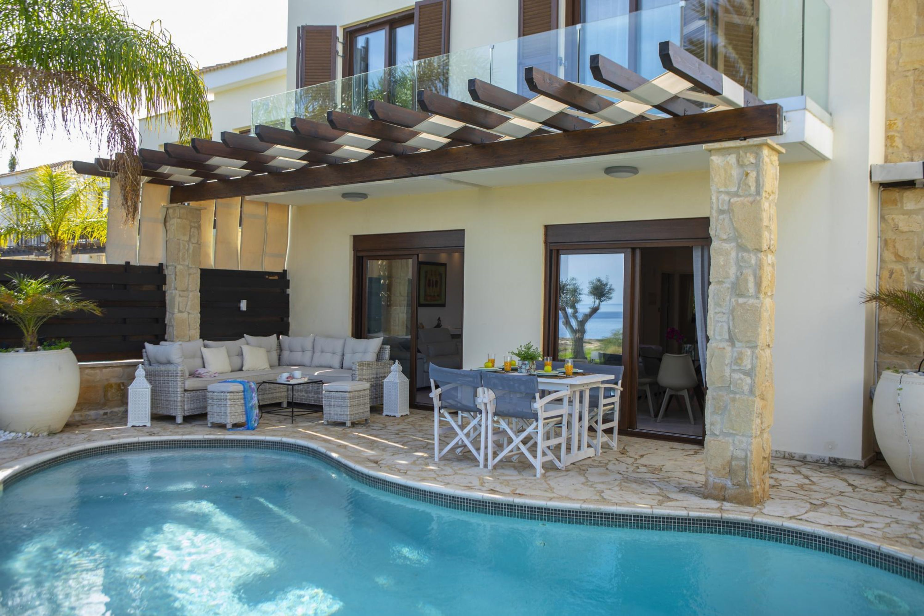 A poolside area with a pergola, outdoor seating, and a view of the sea.