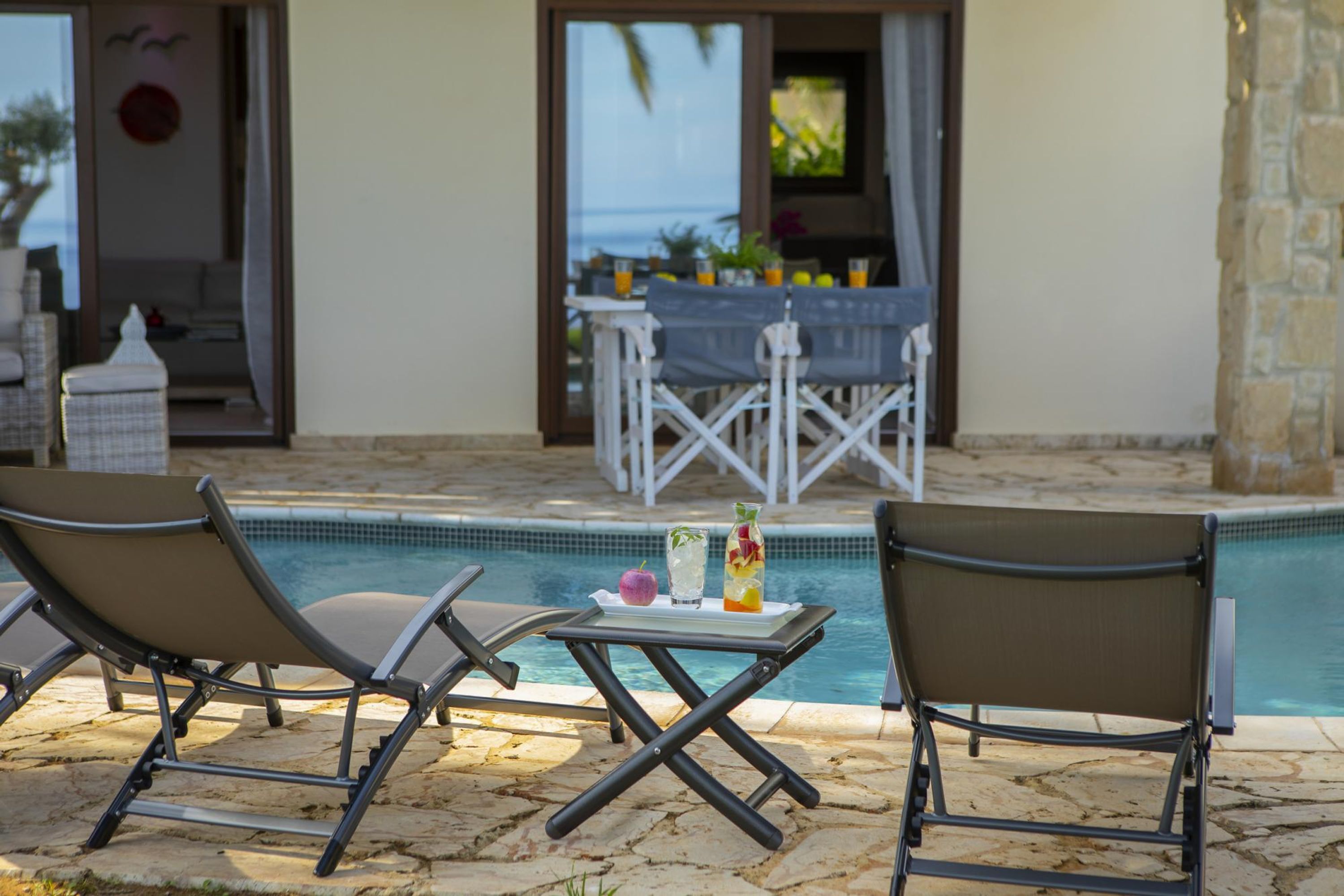 A poolside area with lounge chairs, a table with drinks, and a view of the ocean.