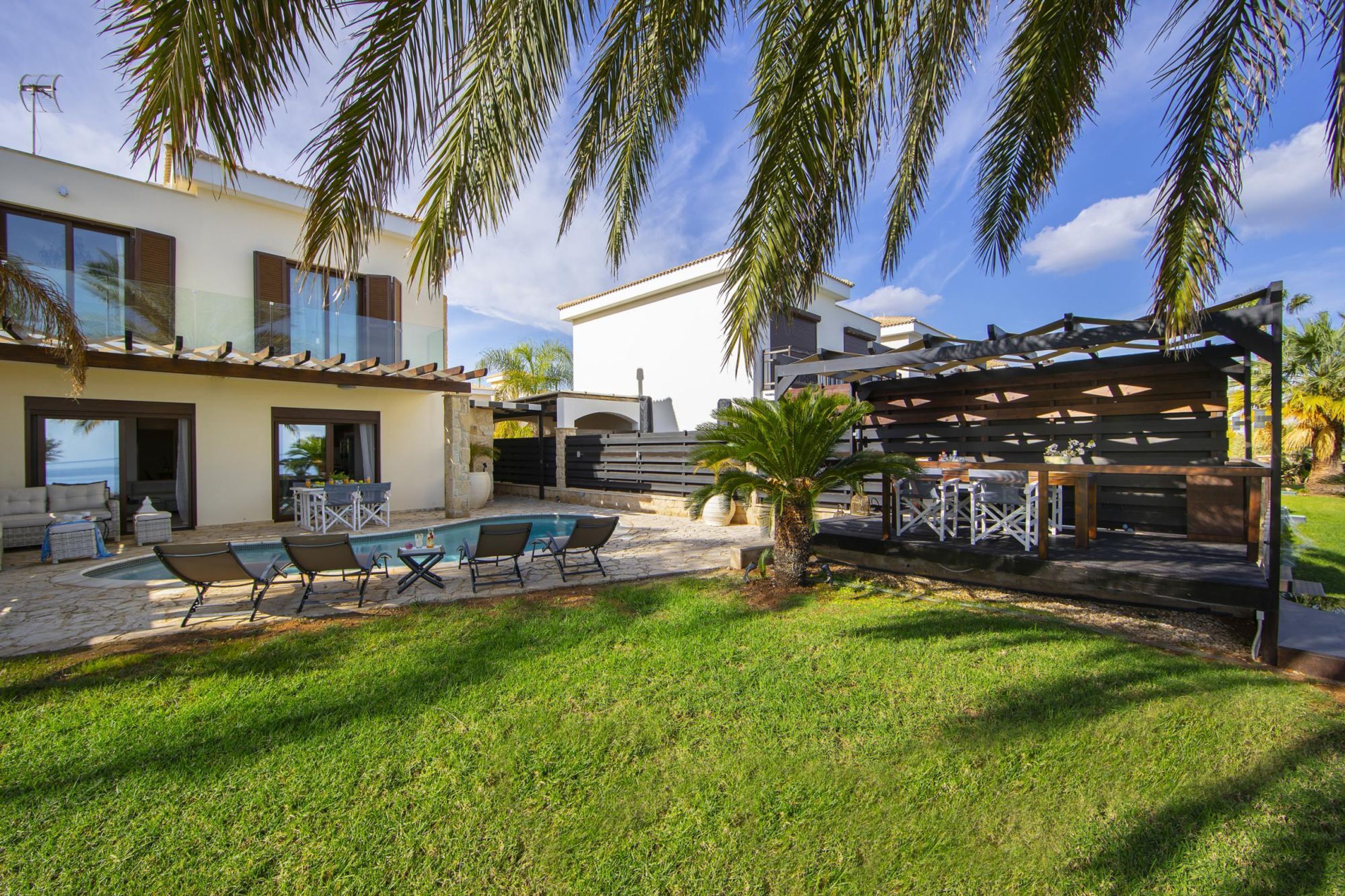 Una casa moderna con piscina, mobiliario exterior y una pérgola.