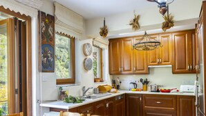 A kitchen with wooden cabinets, a dining table with chairs, a chandelier, and a window with curtains. - Troodos Riverside Cottage (Kato Amiantos)