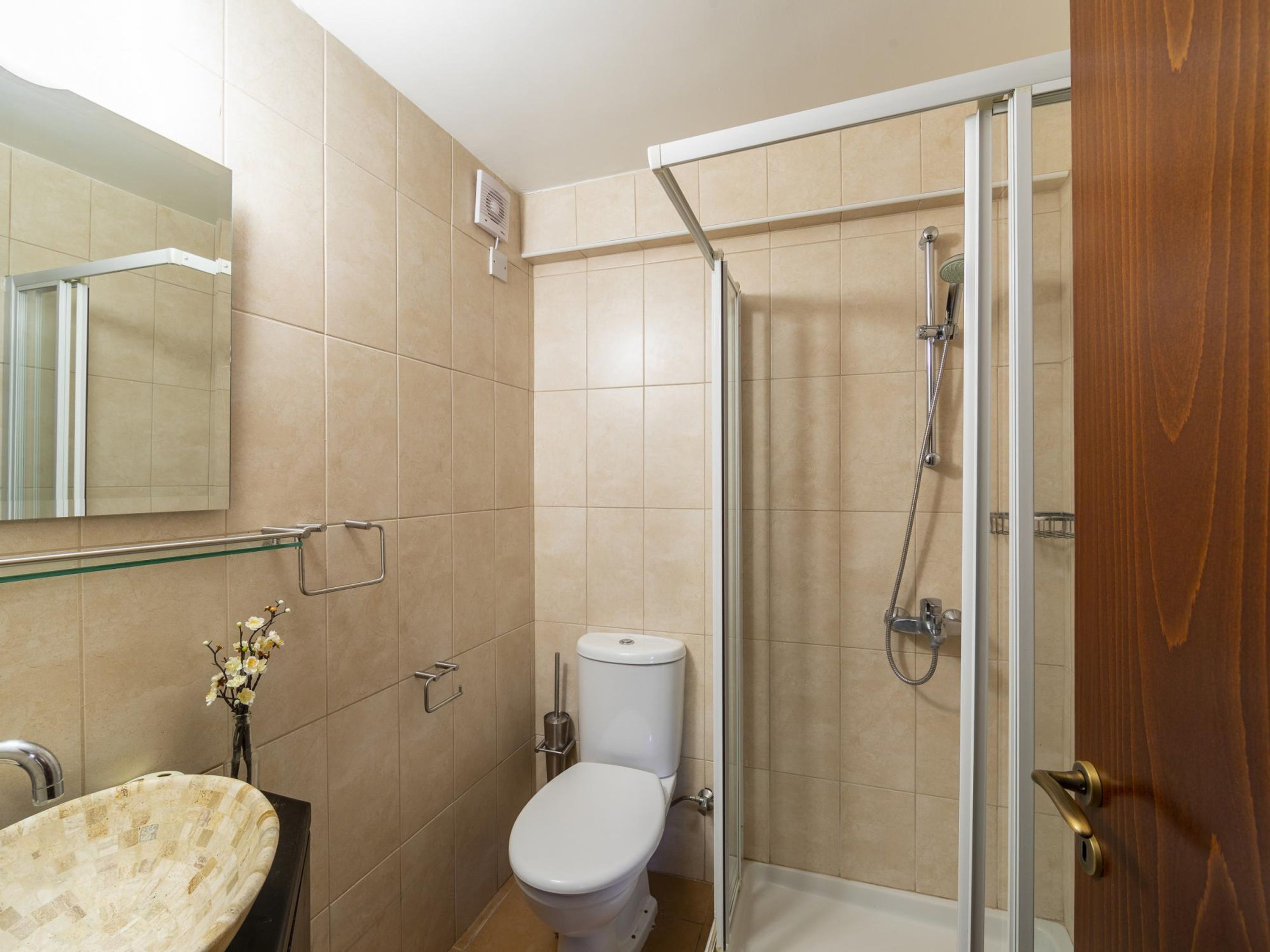 Een badkamer met een douchecabine van glas, een toilet en een wastafel met een bloevas.