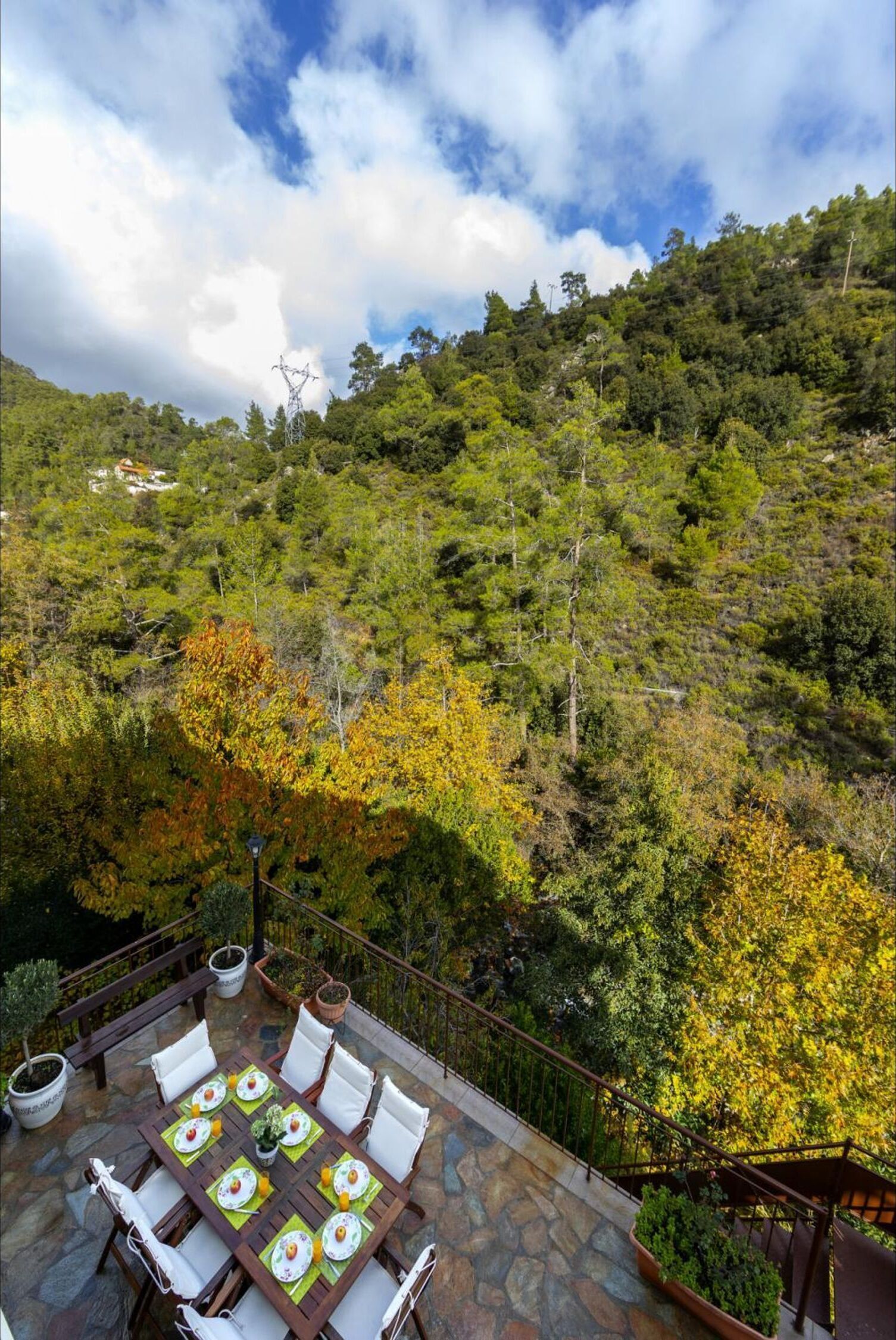 A terrace with a table set for dining, surrounded by lush greenery and a mountainous backdrop.