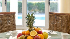 Une table de petit-déjeuner avec des fruits, des croissants et du café, donnant sur une piscine.