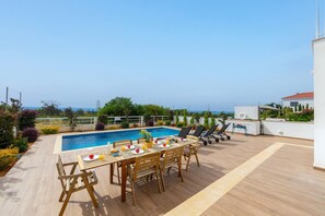 A rooftop pool area with a wooden deck, a dining table set for four, and lounge chairs.
