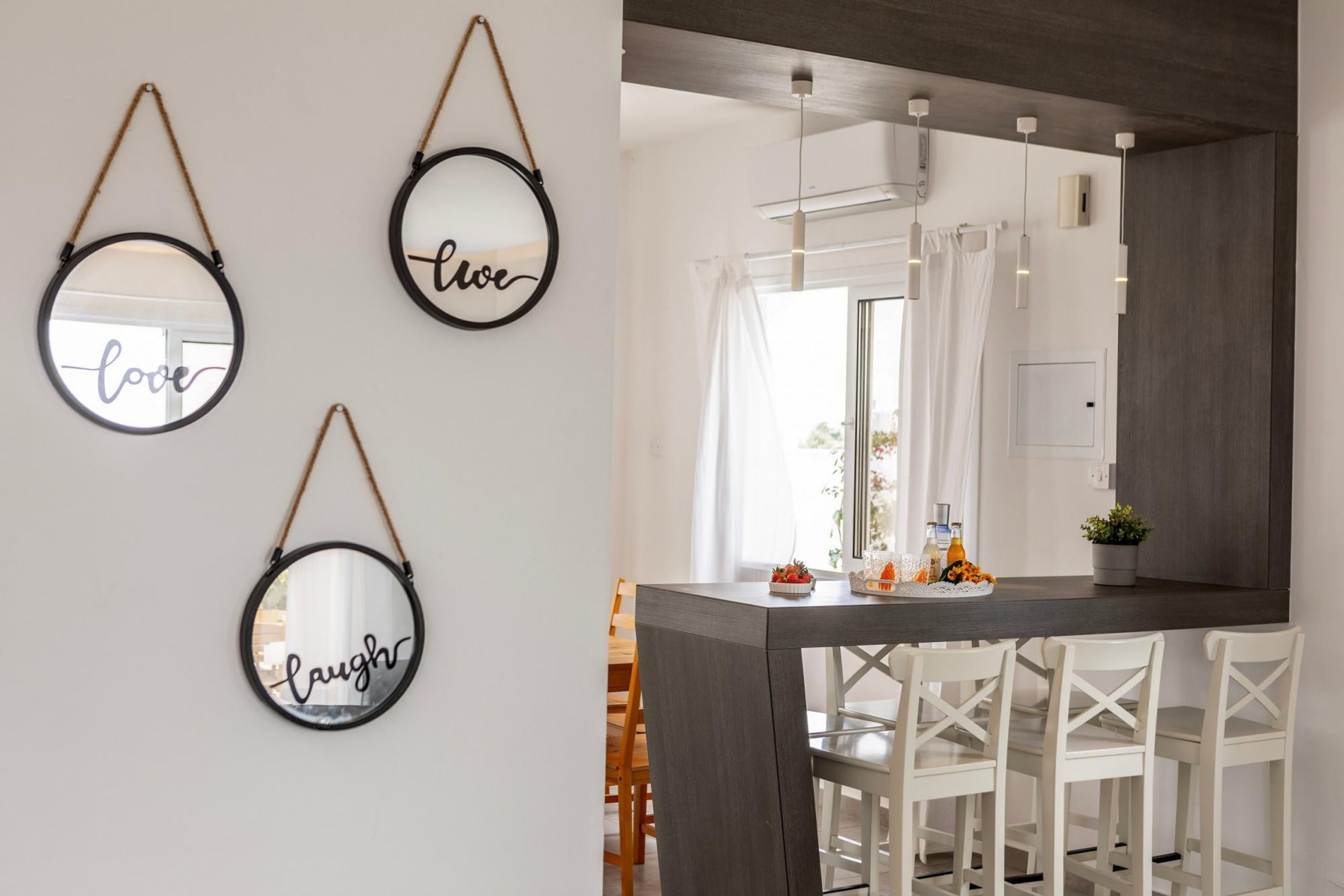Cocina moderna con encimera oscura, sillas blancas y un espejo colgante con la palabra 'love'.