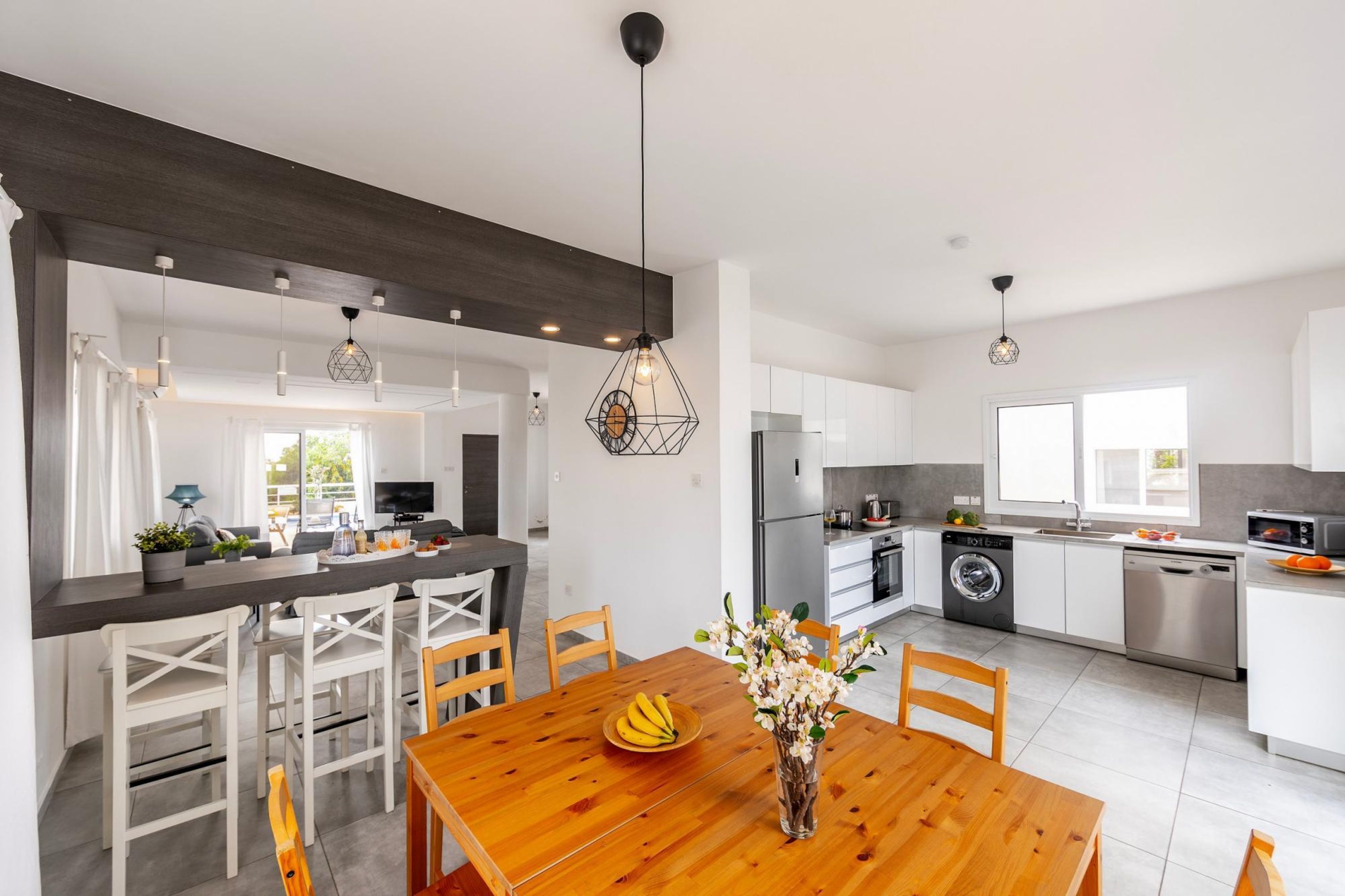 A modern kitchen with white cabinetry, a wooden dining table, and pendant lighting.