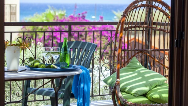 Un balcon avec une table dressée pour deux personnes, une chaise en osier et un fauteuil suspendu avec des coussins.