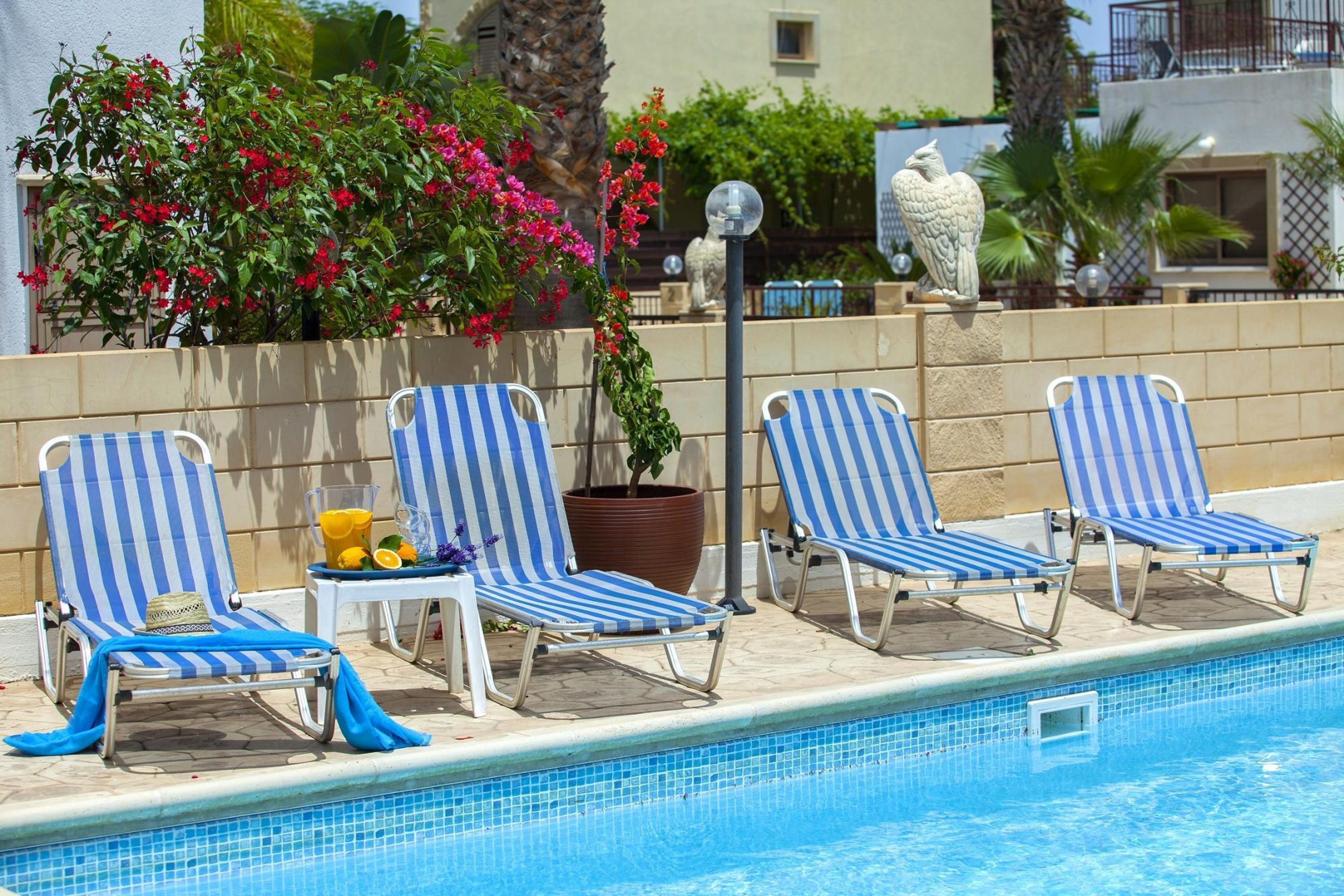 A poolside area with striped lounge chairs, a potted plant, and a statue.