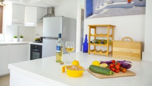 Une cuisine moderne avec un plan de travail blanc, un extracteur de jus, une planche à découper avec des légumes, une bouteille de vin et un verre.