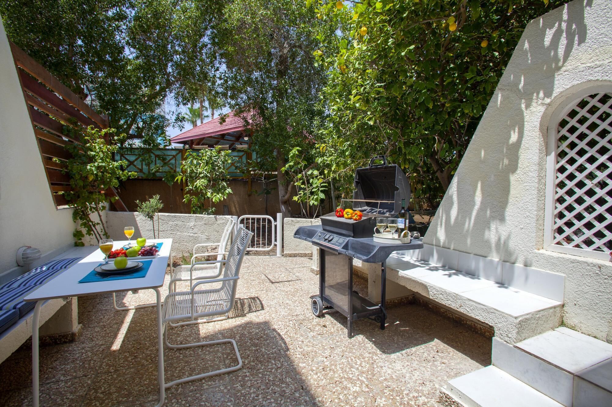 An outdoor patio with a grill, table with chairs, and a small garden area.