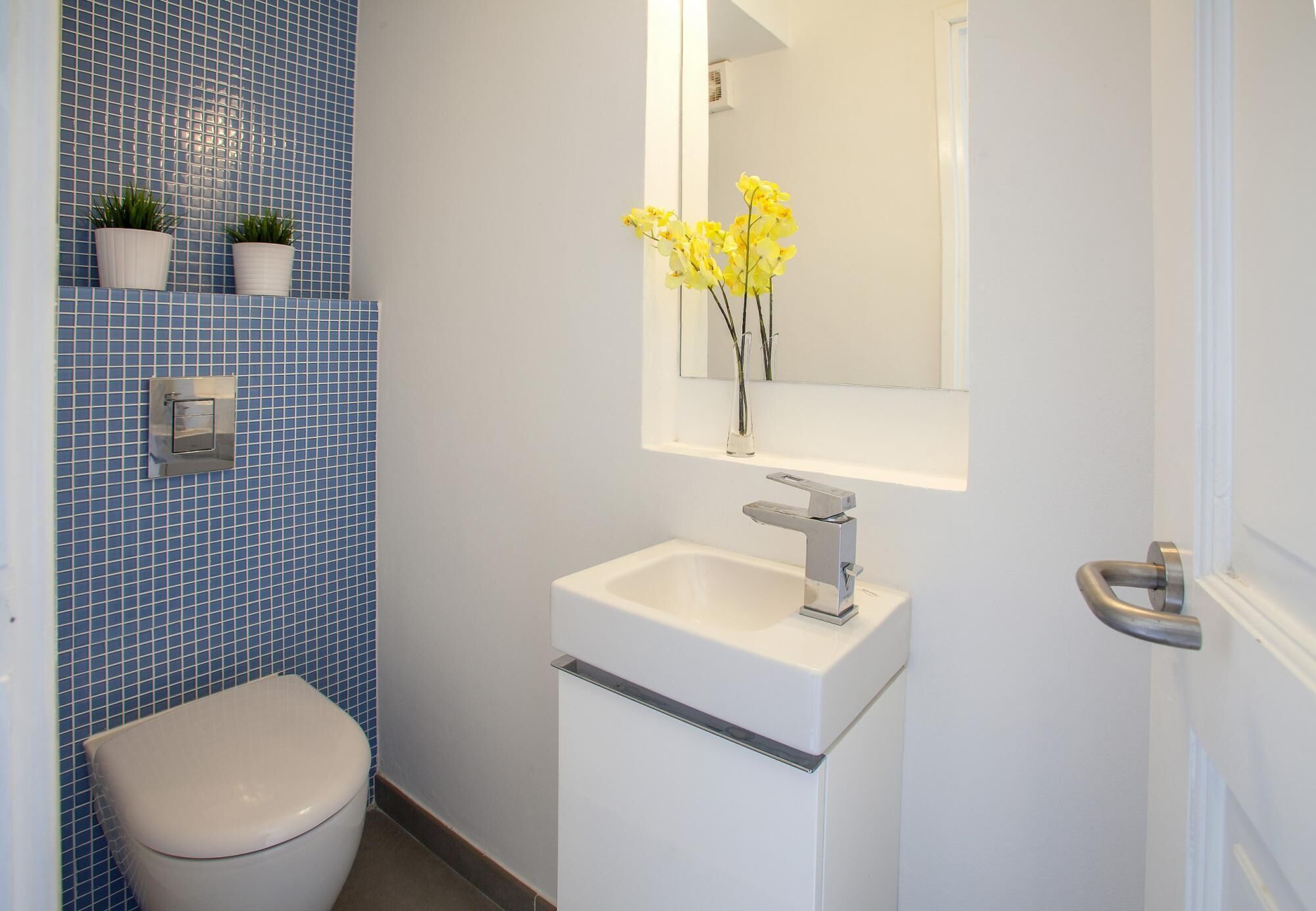 A bathroom with a toilet, a sink, a mirror, and blue tiled walls.