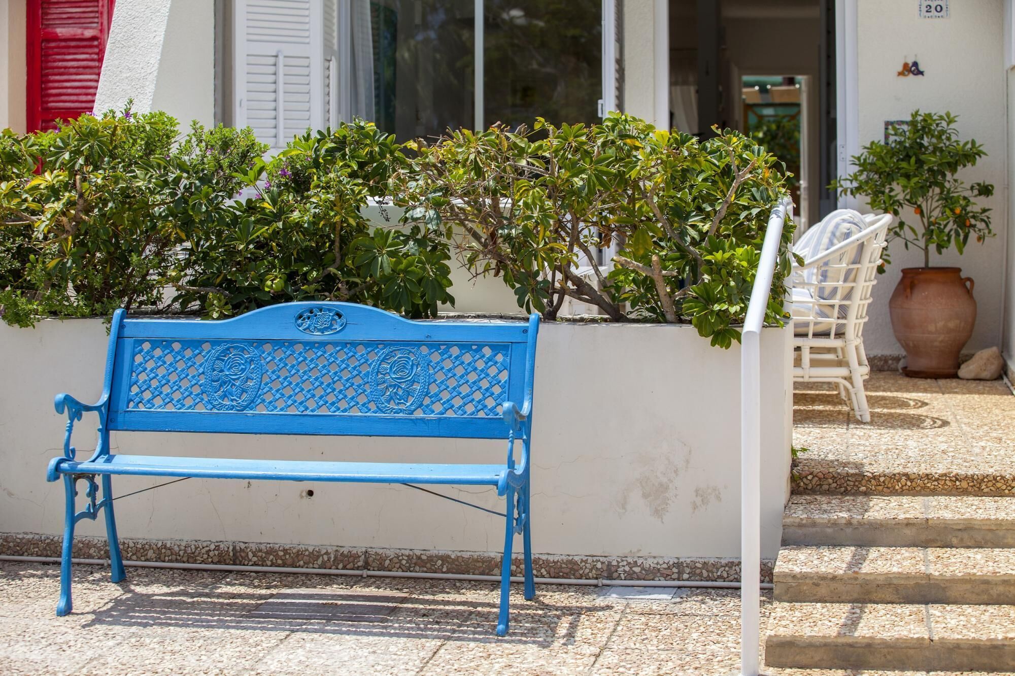 A blue bench outside a building with a white wall and steps leading up to a door.