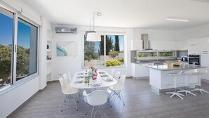 Et moderne køkken med hvide skabe, en central ø og et spiseområde med hvide stole.