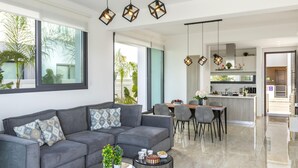 Una sala de estar moderna con un sofá gris, comedor, cocina y ventanas amplias.