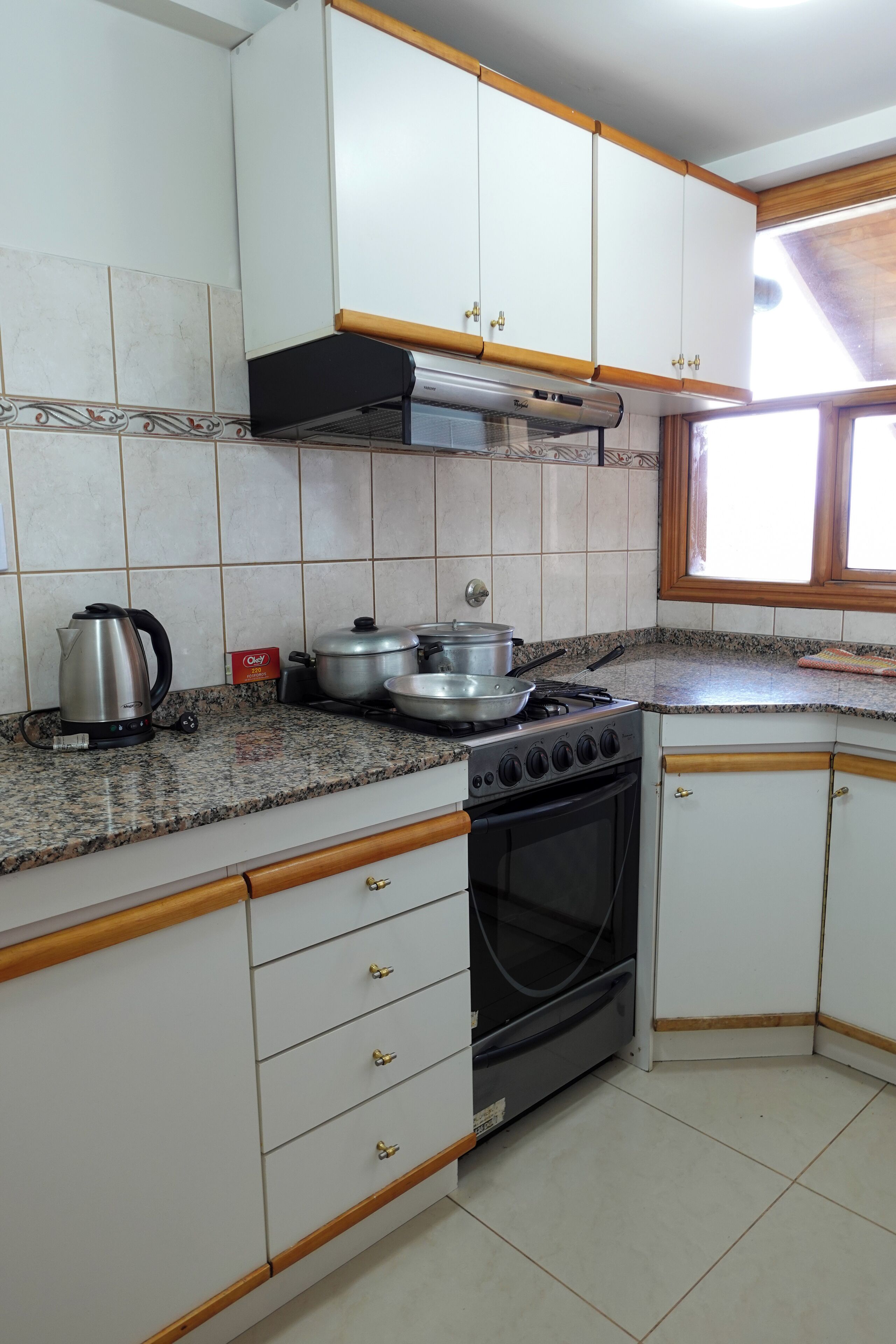 A kitchen with white cabinets, a stove, a kettle, and a window.