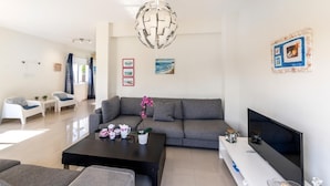 A modern living room with a grey sofa, a black coffee table, and a TV on a white console. - Galleria Sunset Villa (Paralimni)