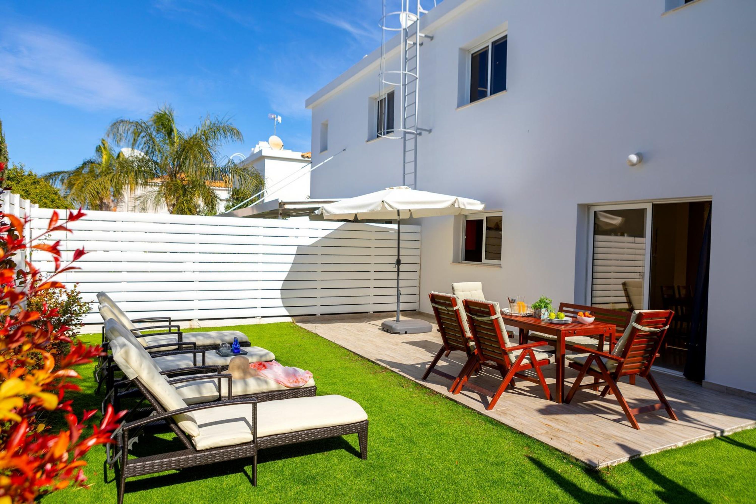 A patio with a dining table, chairs, and a white umbrella.