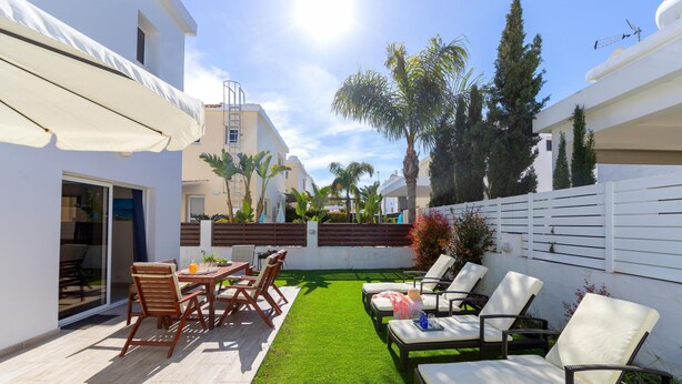 A patio with a dining table and chairs, a grassy area, and lounge chairs. - Galleria Sunset Villa (Paralimni)