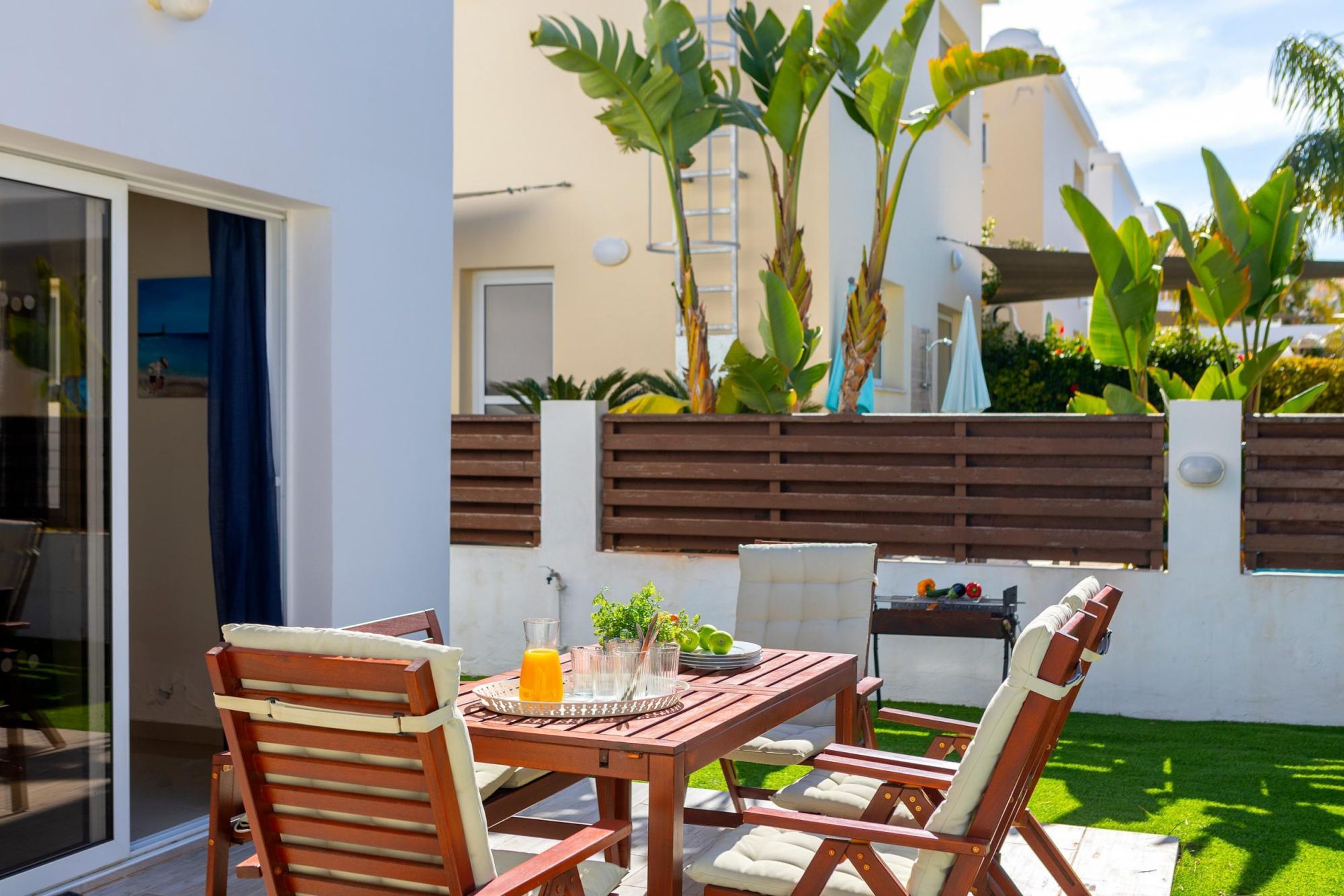 A patio with a wooden table and chairs, a grill, and a variety of plants.