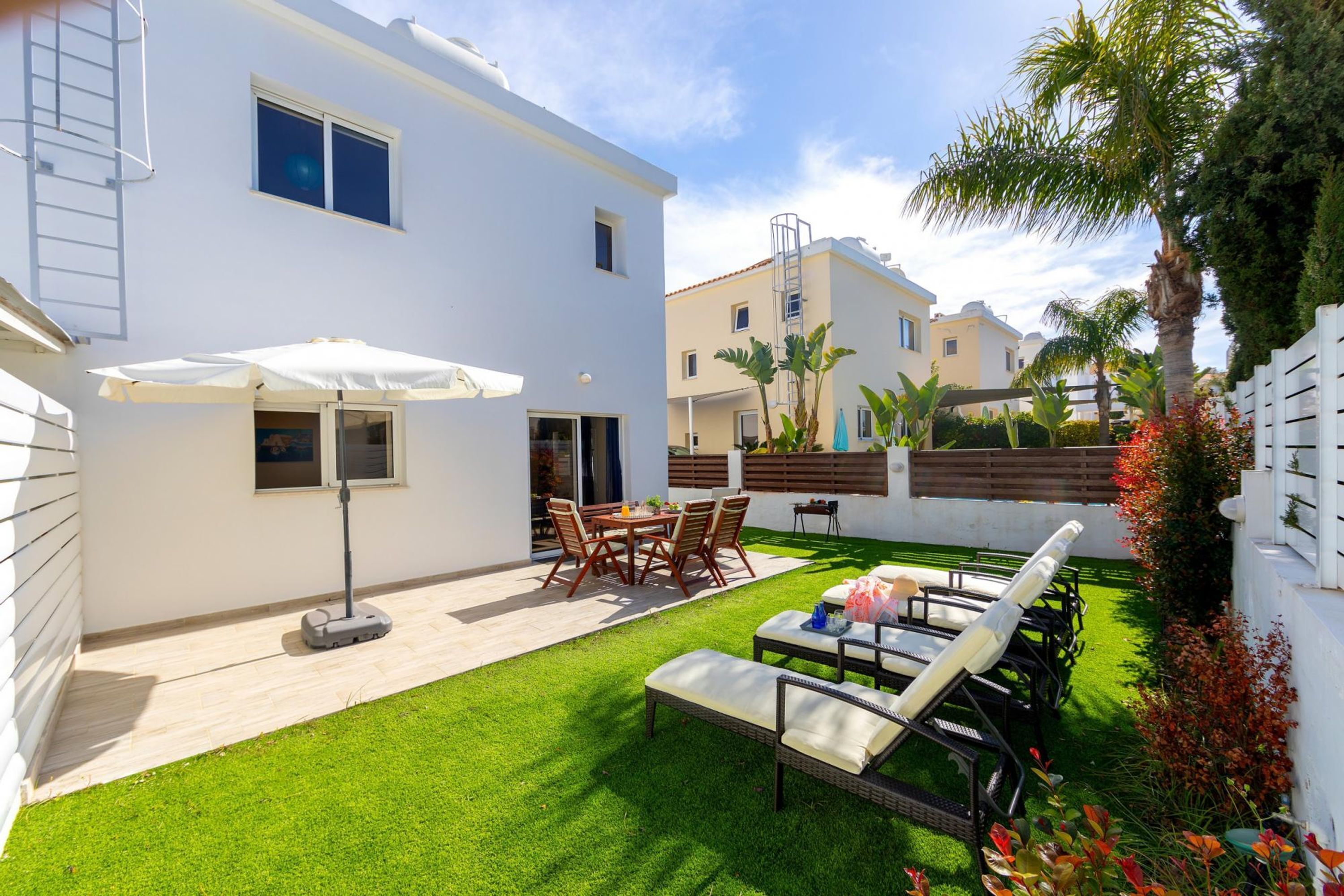 A white building with a patio area featuring a table and chairs, a sun umbrella, and a lounge chair.