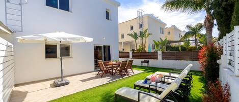 A white building with a patio area featuring a table and chairs, a sun umbrella, and a lounge chair.