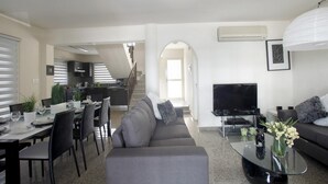 Ein modernes Wohnzimmer mit einem grauen Sofa, einem Essbereich mit einem Glastisch und einer Küche im Hintergrund.