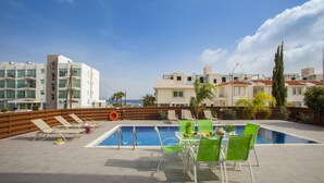 A rooftop pool area with lounge chairs and a table with drinks, overlooking a residential area with modern buildings. - Theodora 16 in Protaras (Paralimni)