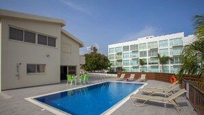 A swimming pool with lounge chairs and a building in the background. - Theodora 16 in Protaras (Paralimni)