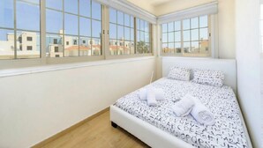 Ein Schlafzimmer mit einem großen Fenster, einem Bett mit alphabetischen Bettbezügen und Blick auf Gebäude.