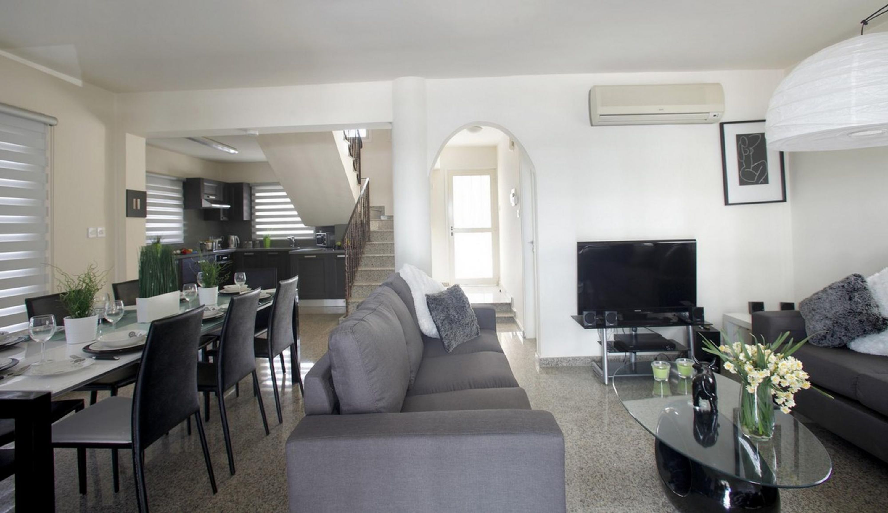 A modern living space with a dining area, sofa, TV, and staircase.