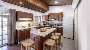 Une cuisine moderne avec des meubles en bois, un îlot central doté de tabourets de bar et une grande fenêtre agrémentée de rideaux.