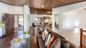 Un salon moderne avec un plafond en bois, un canapé marron, un coin repas et une cuisine en arrière-plan.
