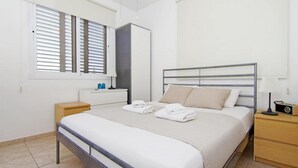 Une chambre bien rangée, avec un lit, des tables de chevet, une armoire et une fenêtre équipée de stores.