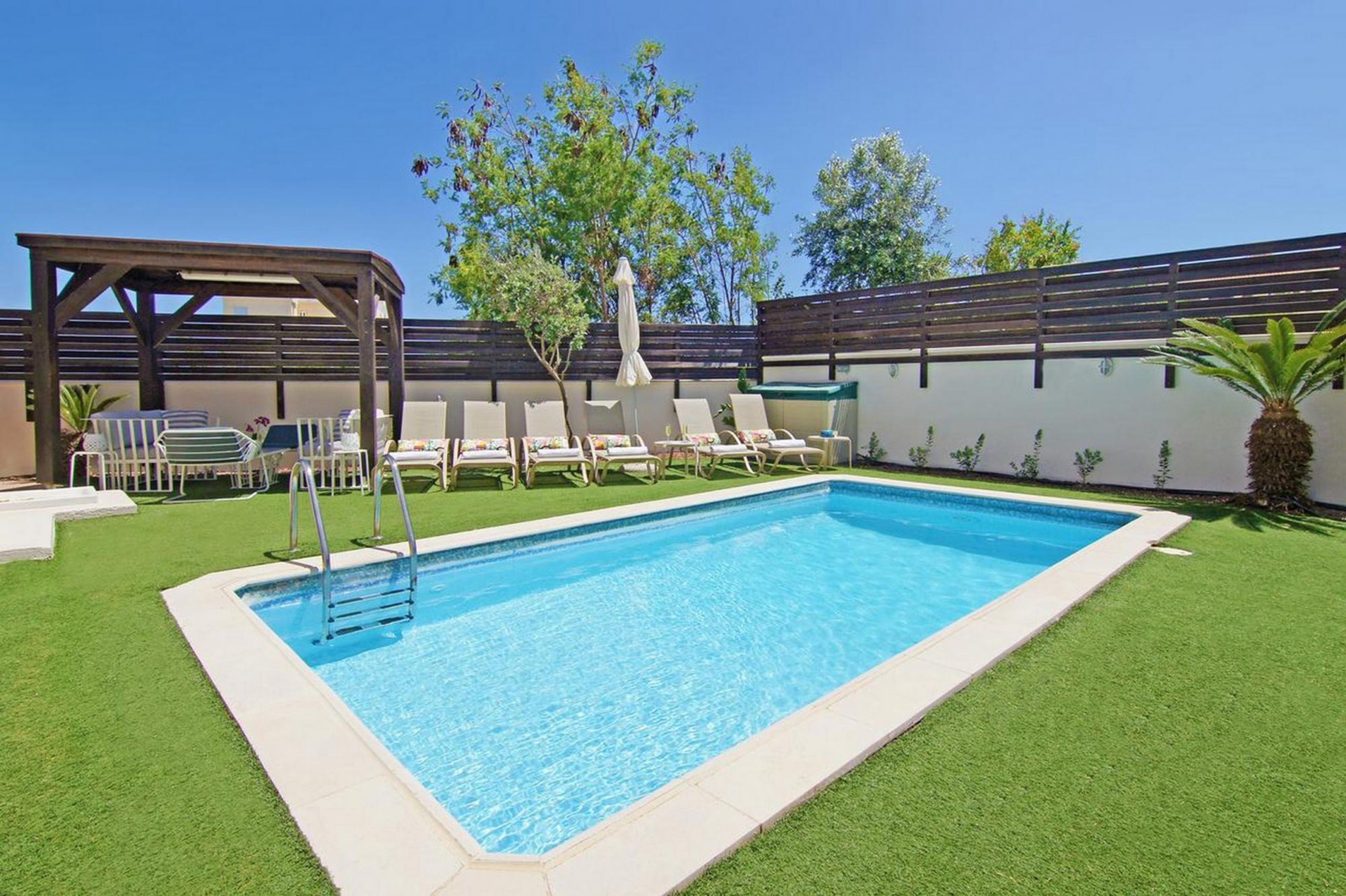 Une piscine rectangulaire dotée d’une terrasse en bois et de chaises longues.