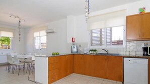Une cuisine moderne avec des meubles en bois, un plan de travail blanc et un lave-vaisselle. On y trouve également un coin repas avec des chaises blanches et une table.