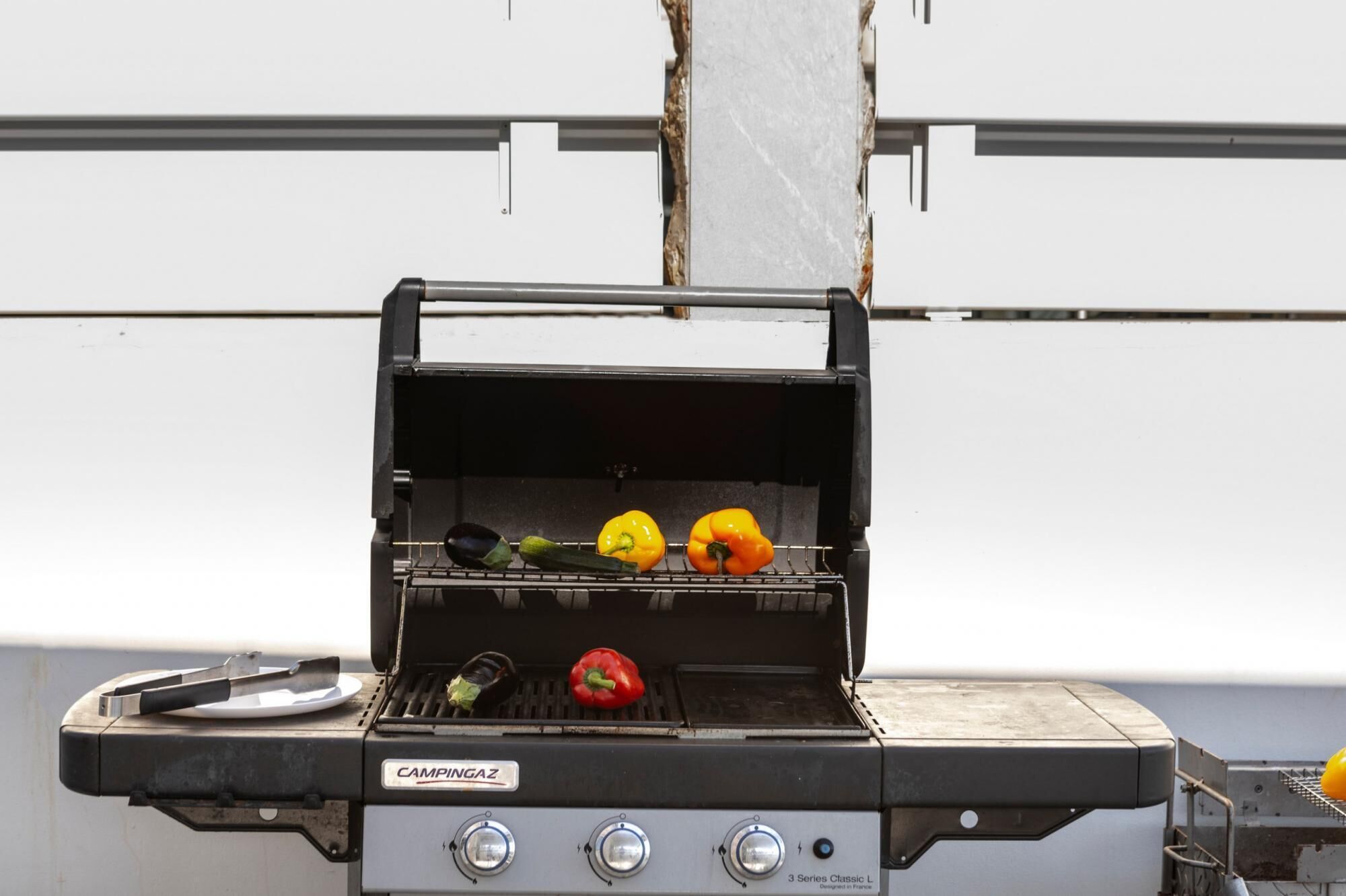 Un barbecue Campingaz avec trois poivrons et une aubergine sur la grille.